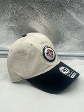 Load image into Gallery viewer, The Winnipeg Jets NHL '47 Brand Natural Two Tone Clean Up Adjustable Strapback Hat displayed next to other team merchandise, showing versatility in fan apparel.