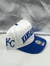 Load image into Gallery viewer, Kansas City Royals MLB '47 Brand White TT Script Hitch Adjustable Snapback Hat displayed on a wooden surface, showcasing its sleek design and iconic Royals logo.