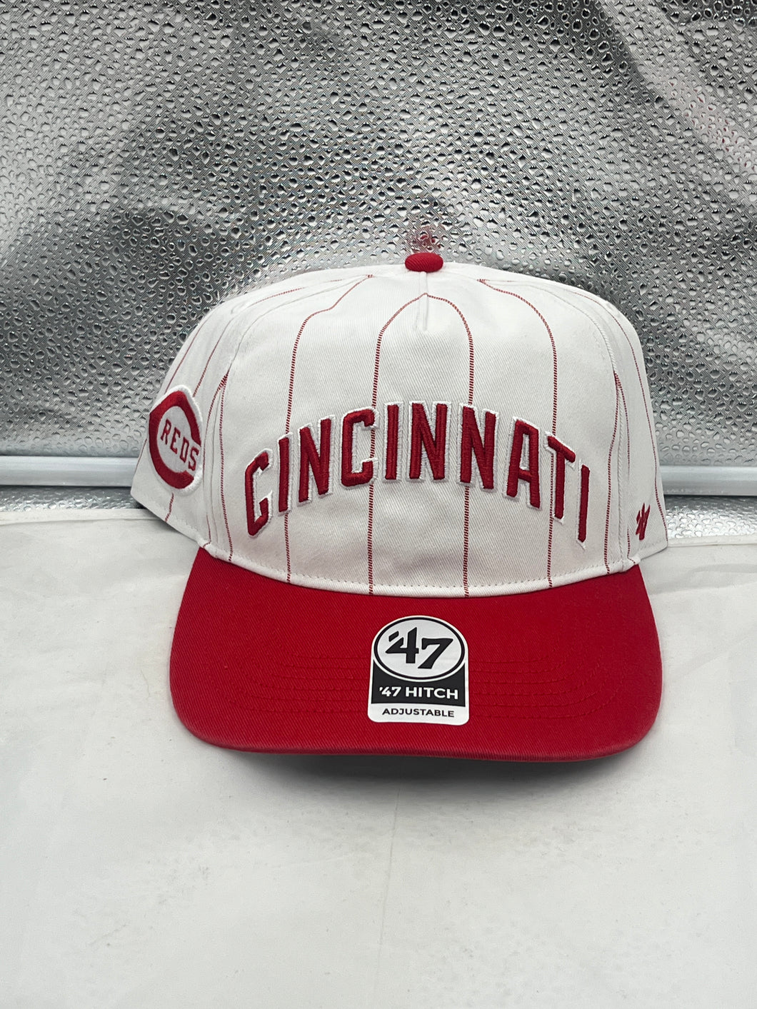Cincinnati Reds MLB '47 Brand White TT Script Hitch Adjustable Snapback Hat displayed on a wooden table with a baseball and gloves in the background.