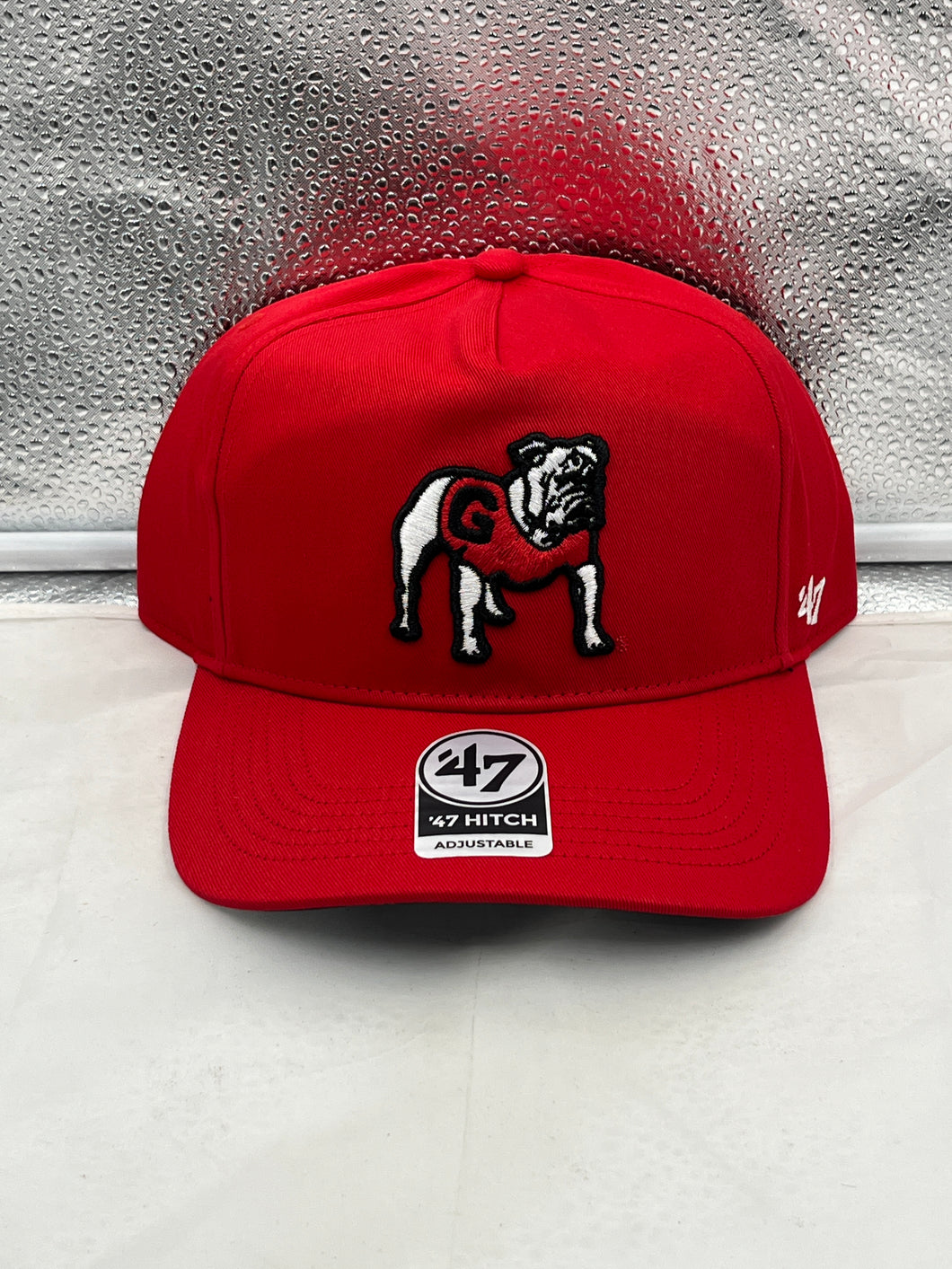Georgia Bulldogs NCAA '47 Brand Throwback Red Hitch Adjustable Snapback Hat displayed on a wooden table with a backdrop of Georgia Bulldogs merchandise.