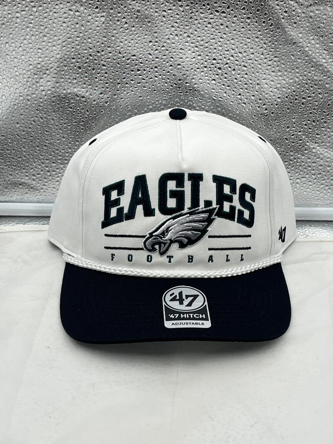 Philadelphia Eagles NFL '47 White TT Roscoe Hitch Rope Snapback Adjustable Hat displayed on a wooden table with a blurred stadium background.