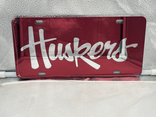 Nebraska Cornhuskers NCAA Red Mirrored Laser Cut License Plate from Craftique, showcasing the team's logo with a vibrant red color and sleek mirrored finish, ideal for sports fans.